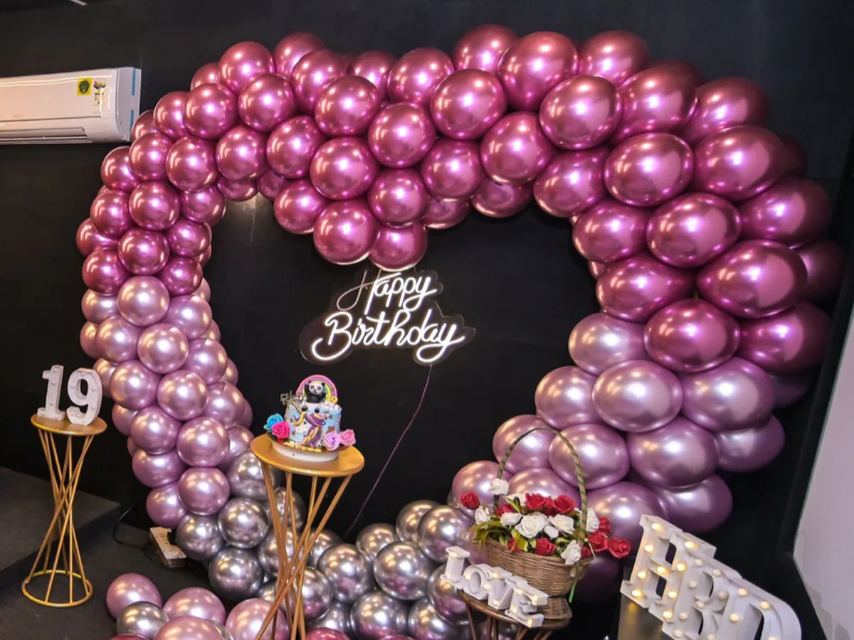 A private theatre set up for a birthday, with a balloon arch, a lit name board and a cake